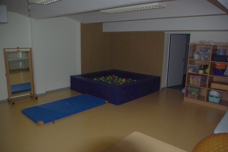 Ein Therapieraum. In der Ecke steht ein Bällebad, davor liegt eine Matte. An der Wand rechts neben dem Bällebad steht ein Regal mit Spielzeugen und Therapiegeräten.
